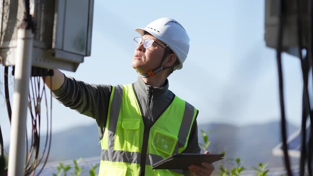 Electricity worker wearing safety helmet checks tablet while inspecting equipment on site
