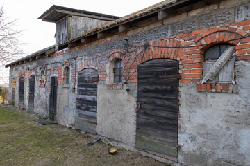 Old brick and concrete barn with weathered wooden doors and arched windows, traditional rural...