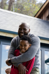 Naklejka premium African American father hugging preteen son, smiling on porch with glass doors, showing wristwatch
