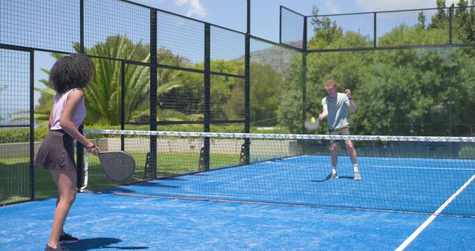 Two players in sportswear exchanging rally after male serve, training with paddles on padel court