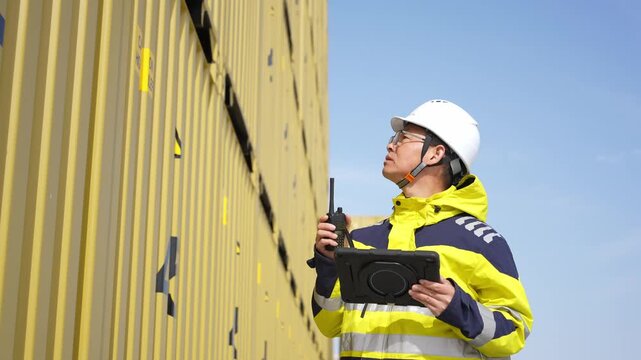 Port worker inspecting shipping containers while holding a tablet device outdoors