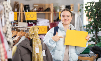 Teenage girl in a clothing store holds a yellow poster with space for text. Joyful teenager on sale in the store. Buying clothes for schoolchildren © JackF