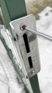 Close-up of a screwdriver unscrewing a rusty screw on a metal gate lock.