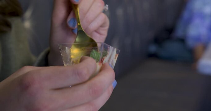 Closeup on woman's hands using spoon to eat pudding in little plastic cup
