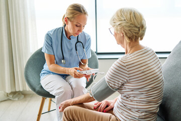 Obraz premium Doctor or nurse caregiver with senior woman using blood pressure tool at home or nursing home