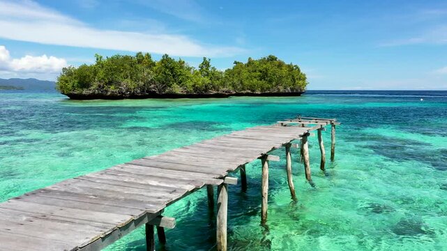 Old wooden jetty over turquoise coral waters with small green islands in Raja Ampat