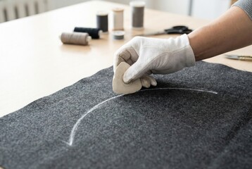 Tailor wearing a white glove marking grey fabric with chalk