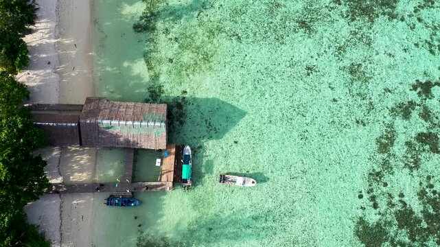 Aerial climb over boats anchored by tropical shore revealing shallow coral bay waters in Raja Ampat