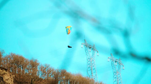Paraglider flying near electricity transmission towers and power lines in the French Alps