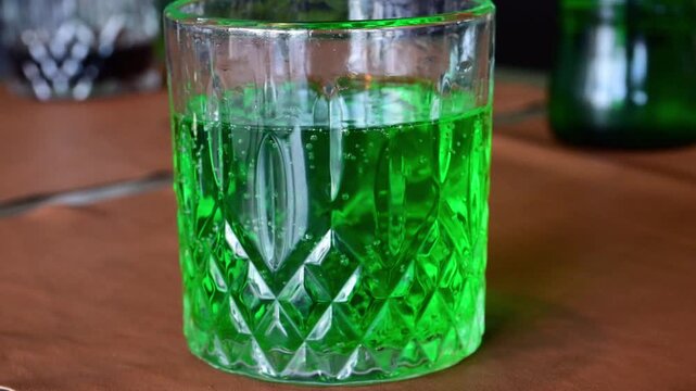 a faceted crystal tumbler filled with a bright, neon green carbonated beverage&mdash;Georgian Tarhun&mdash;showcasing active bubbles rising to the surface,