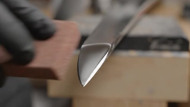 Individual sharpens knife blade using various tools while wearing gloves, showcasing the progression of sharpening techniques in a workshop setting