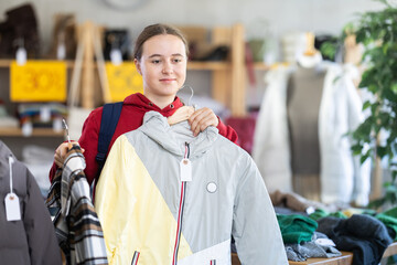 Teenage girl is choosing winter outerwear with interest at a sale in a store, she is holding hangers with jackets and coats © JackF