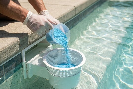 Maintenance worker pouring blue chemical granules into a swimming pool skimmer