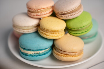 Fototapeta premium studio close-up of a stacked assortment of pastel french macarons on a white plate set on a neutral tabletop, showcasing delicate crisp shells, creamy fillings, soft textures, gentle light, and inviti
