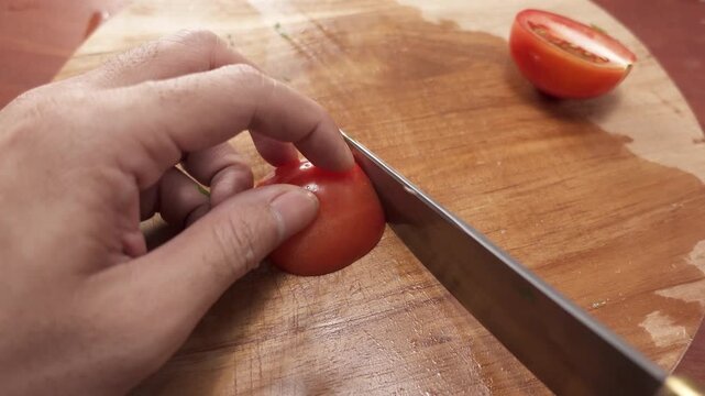 Close-up of slicing ripe red tomatoes into thin slices with a kitchen knife on a cutting board, preparing fresh and healthy ingredients for cooking