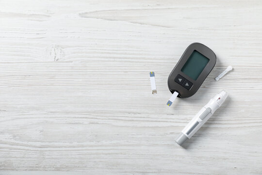Diabetes. Digital glucometer with test strip, pen and lancet on white wooden table, flat lay. Space for text
