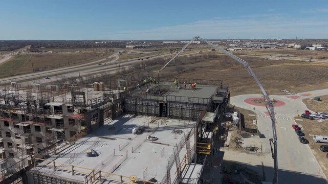 Fort Worth, Texas USA &ndash; February 18, 2026: Construction workers on the top level of a multi-story building under construction while a concrete pump truck pours concrete at the site.