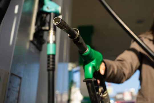 Hand holding gasoline nozzle at fuel station close-up. Driver refueling car using gasoline pump