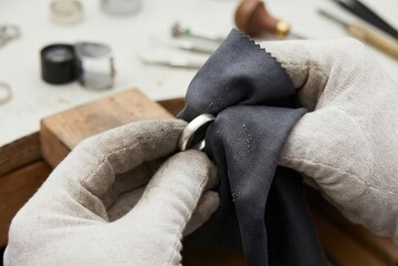 Jeweler hands in gloves polishing silver ring with dark microfiber cloth on workbench