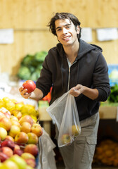 Obraz premium Young man buyer choosing fresh apples in vegetable shop