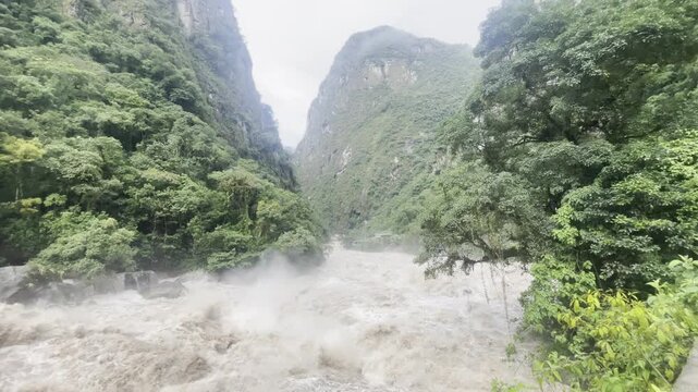 A swollen brown river rushes through a sharp bend on the Andean slopes near Machu Picchu and Cusco, powerful muddy water carving its path through the mountain landscape. Filmed in Peru.