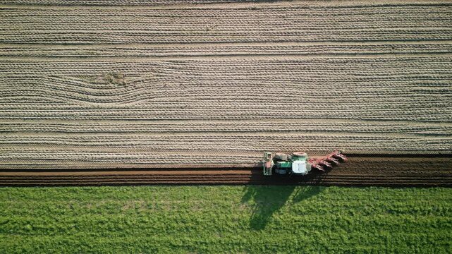 Tractor with trailer plowing field in spring, top drone view