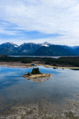 Obraz premium Small Island and Lake Reflection With Mountain Range and Forested Shoreline in BC Canada