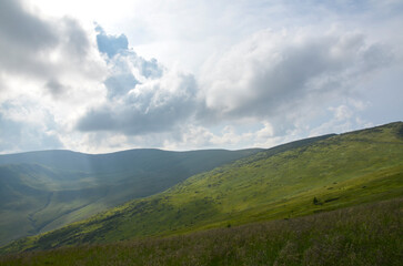 Vast green mountain meadow slopes toward rolling hills beneath a dramatic cloudy sky, evoking calm, freedom and wide open summer landscape scenery. Carpathian Mountains, Ukraine