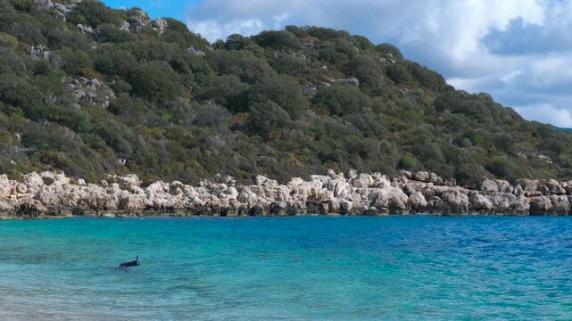 Scuba diver emerging from turquoise water near rocky coast. Crystal-clear turquoise water gently laps against a rocky coastline as a scuba diver surfaces