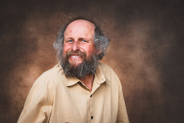 Porträt eines lächelnden älteren Mannes mit Vollbart und lockigem Haar vor braunem Hintergrund.