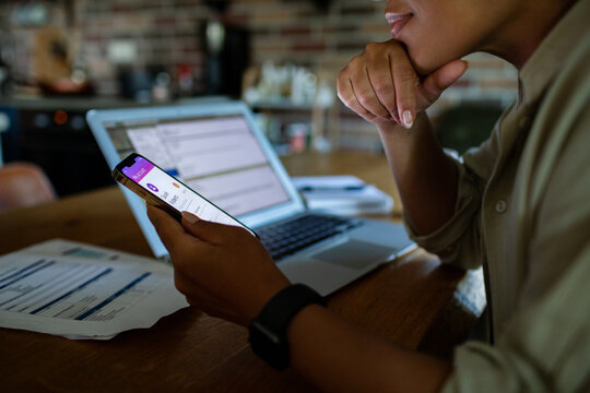 Adult managing finances on mobile banking app at kitchen table