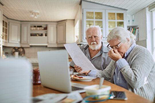 Worried senior couple reviewing bills at kitchen table