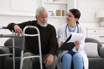 Obraz premium Care worker with clipboard talking to senior man indoors