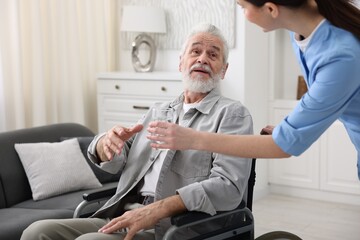 Obraz premium Care worker giving glass of water to senior man in wheelchair indoors