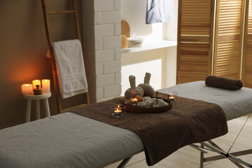 Herbal sacks, rocks and burning candles on massage bed in spa center