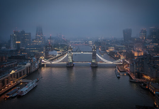 Moody view of the lit up Tower Bridge in London, UK, with heavy fog during evening time