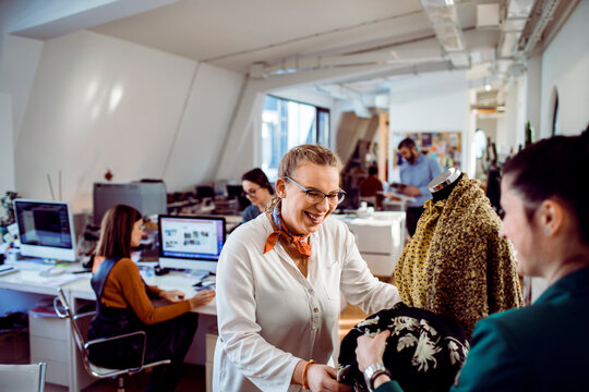 Two female fashion designers reviewing fabrics on mannequin in modern studio office