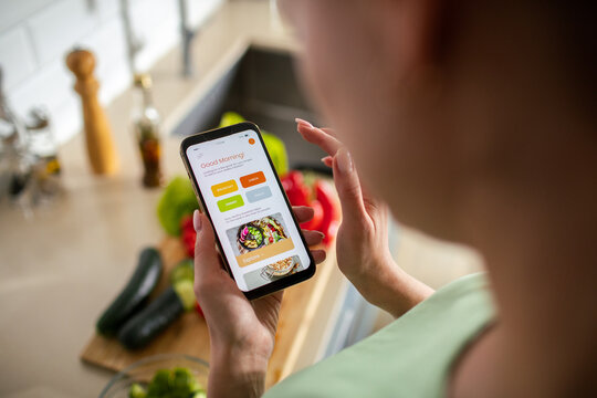 Woman using recipe app on smartphone in home kitchen