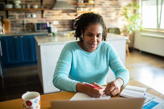 Smiling woman taking notes on a video call in a home kitchen