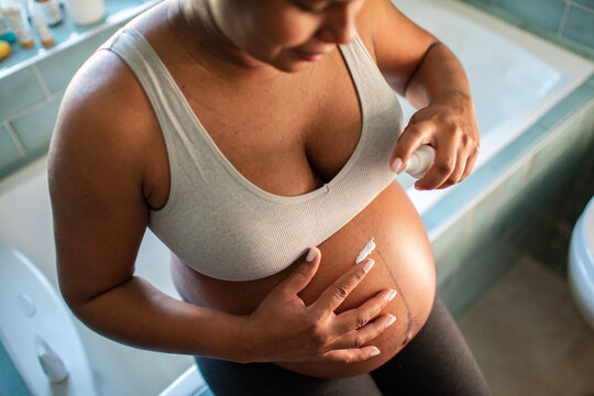 Pregnant woman applying belly lotion in bathroom