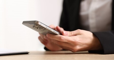 Woman sending text message via smartphone at wooden desk indoors, closeup