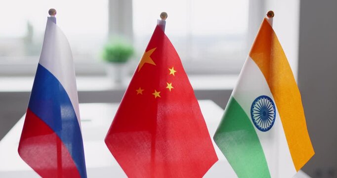 Diplomacy flags highlight negotiation and trilateral cooperation. Three small national flags stand side by side on an office table, suggesting coordinated talks. Concept: trilateral dialogue.