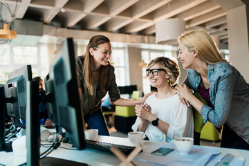Fototapeta premium Three female coworkers celebrating success in modern office