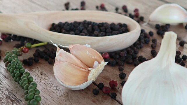 Black peppercorns, green peppercorns, red peppercorns, and garlic are placed on the wooden floor.