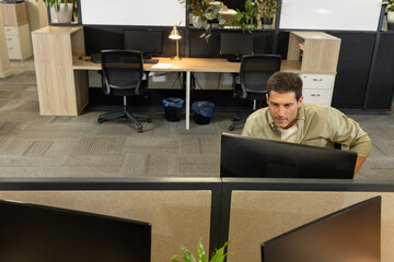 Mature man leaning forward viewing computer monitors at open-plan office cubicle with plants © wavebreak3