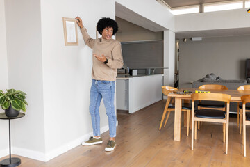 Hanging man wearing turtleneck placing framed artwork on wall at home with spirit level, copy space © wavebreak3