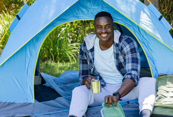 African American man sitting at tent in flannel holding mug reaching for food container © wavebreak3