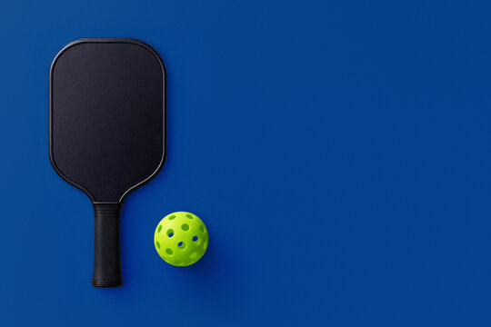 Pickleball paddle and yellow perforated ball on blue background. Sports equipment, active lifestyle and minimalist pickleball competition concept