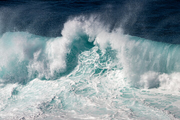 Naklejka premium An angry turquoise green color, massive rip curl of a wave as it rolls along a beach. The white mist and froth from the wave are foamy and fluffy. The Atlantic Ocean in the background is deep blue. 