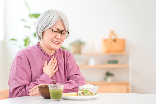 A gray-haired senior woman choking while eating (aspiration pneumonia, swallowing disorder)